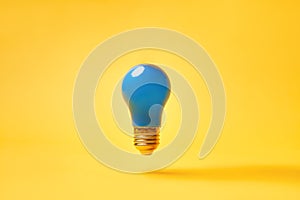 Blue lightbulb levitate on yellow background. Idea and inspiration concept