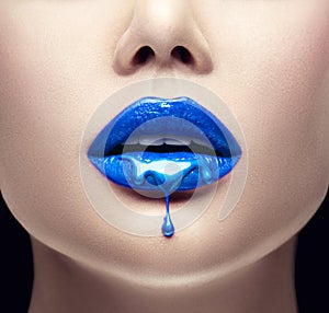 Blue lipstick dripping. Lipgloss dripping from lips, Blue liquid drops on beautiful model girl`s mouth, creative makeup photo