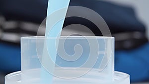 Blue liquid laundry detergent is poured into a palstic measuring cap