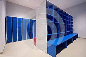 Blue lockers on a wall and cabinet with empty shelves with the bench