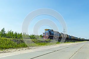 A blue locomotive tows a fuel tanks wagons against a blue sky.