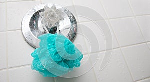 A blue loofah sponge hanging in a wet shower on the temperature guage