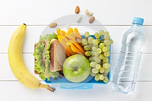 Blue lunch box with healthy food for school children with bottle of water on white wooden background.