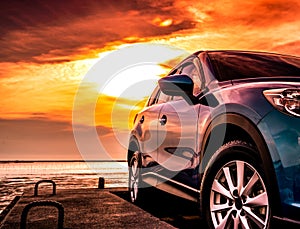 Blue luxury SUV car parked on concrete road by sea beach with beautiful red sunset sky. Summer vacation at tropical beach. Road