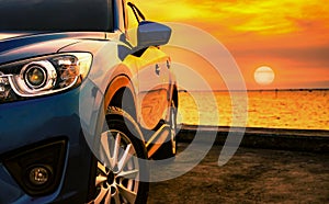 Blue luxury SUV car parked on concrete road by sea beach with beautiful red sunset sky. Summer vacation at tropical beach. Road