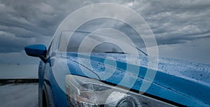 Blue luxury SUV car with water drops parked on road beside sea beach on rainy day with storm sky. Raindrops on blue SUV car. Road