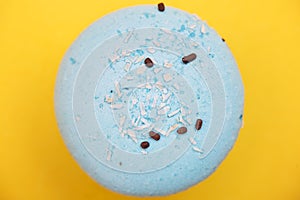 Blue macaron with coconut shavings and chocolate on yellow backgroundn