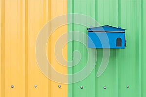 Blue mail box on orange and green corrugated metal sheet as back