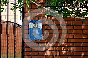 A blue mailbox hangs on the fence. Number 20. Red brick and birch are visible