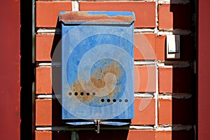 A blue mailbox hangs on a red brick wall outside. Russian post box