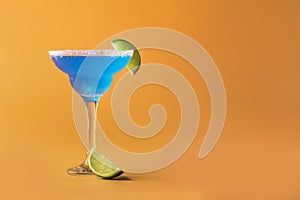 Blue margarita alcoholic cocktail with tequila, liqueur, lime juice, salt and ice, summer yellow background, copy space