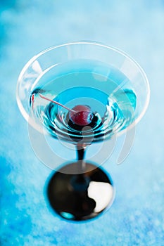 Blue martini cocktail with cherry on the rustic background