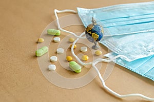 Blue medical disposable protective mask, small globe and a scattering of tablets on a light background. Coronavirus concept