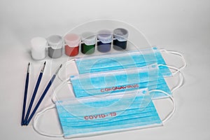 Blue medical masks lie on a white background together with paints for painting and brushes.