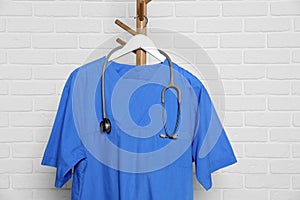 Blue medical uniform and stethoscope hanging on rack near white brick wall