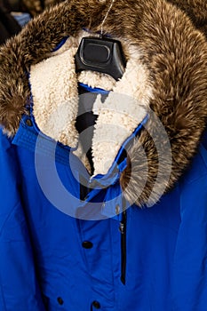 A blue men's sheepskin fur-lined jacket with a fluffy fur hood hangs in a men's clothing store.