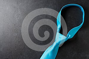 Blue men`s tie on a black concrete background. The concept of a successful modern man. Copy space