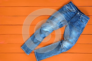 Blue mens jeans denim pants on orange background. Contrast saturated color. Fashion clothing concept. View from above