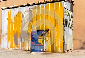 Blue metal drum in front of a shed painted in white and yellow. Text on the door: Dye house photo