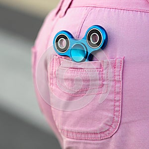 Blue metal popular fidget spinner in the back pocket of pink jeans shorts, anxiety relief toy, anti stress and relaxation fidgets