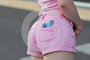 Blue metal popular fidget spinner in the back pocket of pink jeans shorts, anxiety relief toy, anti stress and relaxation fidgets