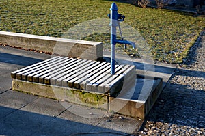 Blue metal retro well with polished elegant wooden lid. water flows from the hand pump into the stone trough. garden bench shaped