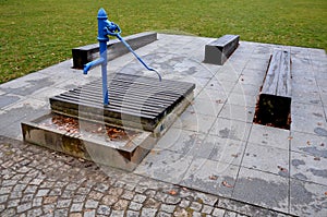 Blue metal retro well with polished elegant wooden lid. water flows from the hand pump into the stone trough. garden bench shaped