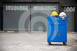 Blue metal tool cabinet with safety helmets, glove, document pad on the cabinet with garage background. Automobile repair service