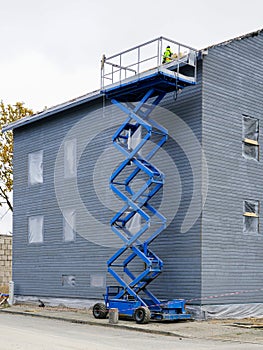 A blue mobile scissor lift platform high elevated next to the grey facade of a residential building