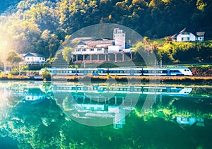 Blue modern high speed train and river in green forest at sunrise