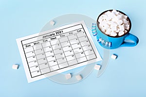 Blue monday concept. Blue mug of cocoa with marshmallows and calendar on blue background