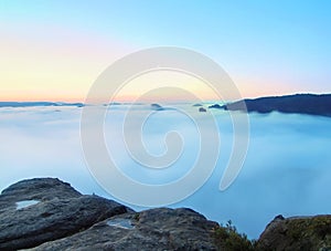 Blue morning, view over rock to deep valley full of light mist. Dreamy spring landscape within daybreak