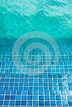 Blue mosaic tiled steps in green swimming pool