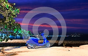 Blue Motor bike at Patong Beach Phuket Thailand at night. Lush green trees in the background white sandy beach.