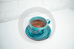 Blue mug with black coffee with a saucer on a white table. Top view