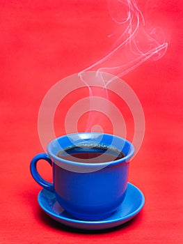 Blue mug with hot coffee steaming. Soft smoke. Red background.