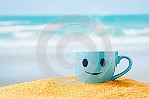 blue mug of hot coffee or tea on sand beach .