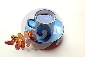 Blue mug on a plate with hot tea and autumn leaf on a light background, side view - the concept of bright autumn days