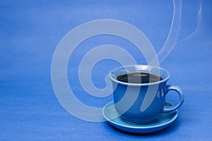 Blue mug with steaming hot coffee. Soft smoke. Blue background.