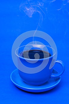 Blue mug with steaming hot coffee. Soft smoke. Blue background.