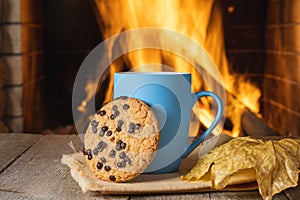 Blue mug of tea or coffee before a cozy fireplace, in a country house, autumn or winter holidays