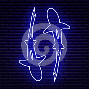 Blue neon sign, two sharks top view. Floating around. Against the background of a brick wall with a shadow.