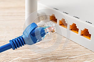 Blue network cable plug almost inserted into the yellow socket of white wi-fi wireless router. Wlan router for home and office for