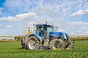 Blue modern tractor pulling a chafer crop sprayer