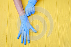 Blue Nitrile gloves. Hands of a medic in the blue latex gloves on a yellow wooden background with place for your text