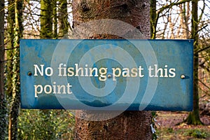 Blue no fishing past this point sign on a tree in a woodland beside the water