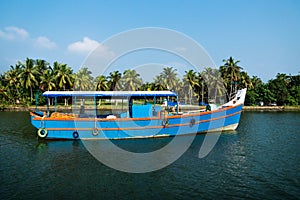 Blue ocean fishing boat along the canal Kerala backwaters shore with palm trees between Alappuzha and Kollam, India photo