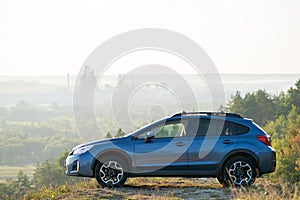 Blue off road car at dawn on grassy hill on distant foggy city landscape background. Extreme travel on a SUV automobile