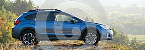 Blue off road car at dawn on grassy hill on distant foggy city landscape background. Extreme travel on a SUV automobile