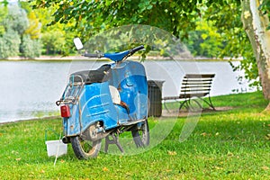 Blue old motorcycle at the lakeshore with trees and bench